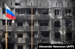 Российский флаг на фоне разрушенного здания в Мариуполе