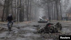 Mještani prolaze biciklima pored uništenih automobila, Buha, Ukrajina, 1. april