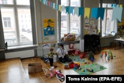 Волонтер играет с украинскими детьми-беженцами в Украинском центре поддержки в бывшем здании Рижского технического университета (РТУ). Апрель 2022 года