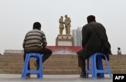 Отец и сын, уйгуры, в центре местной столицы Урумчи смотрят на огромную статую "Мао встречает уйгура"