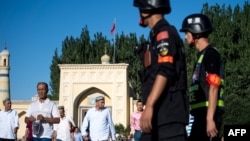 Китайские полицейские наблюдают за уйгурами, выходящими после молитвы из мечети Ид Ках в городе Кашгар. 2019 год