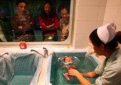 Члены китайской семьи смотрят, как медсестра купает родившегося у одной из их родственниц младенца