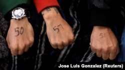 Люди, надеющиеся подать заявление властям США о предоставлении убежища, показывают руки с нарисованными ручкой цифрами, чтобы зарезервировать места в очереди на границе на международном мосту между Мексикой и США в мексиканском городе Сьюдад-Хуарес