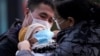 Родители надевают ребенку медицинскую маску у входа на вокзал в Шанхае