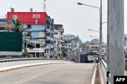 A Myanmar flag (R) flutters atop a Border control building on the Myanmar side as Myanmar nationals walk on the Thailand-Myanmar Friendship bridge, as seen from Thailand's Mae Sot district on April 12, 2024.