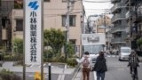 Seorang perempuan mengarahkan jarinya ke papan nama Kobayashi Pharmaceutical saat berjalan melewati kantor perusahaan tersebut di Tokyo, 28 Maret 2024. (Yuichi YAMAZAKI / AFP)
