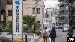 Seorang perempuan mengarahkan jarinya ke papan nama Kobayashi Pharmaceutical saat berjalan melewati kantor perusahaan tersebut di Tokyo, 28 Maret 2024. (Yuichi YAMAZAKI / AFP)