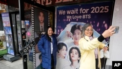 Seorang perempuan berswafoto di depan foto anggota grup K-Pop BTS di sebuah kafe di Seoul, Korea Selatan, 11 Desember 2023. (Foto:Ahn Young-joon/AP Photo)