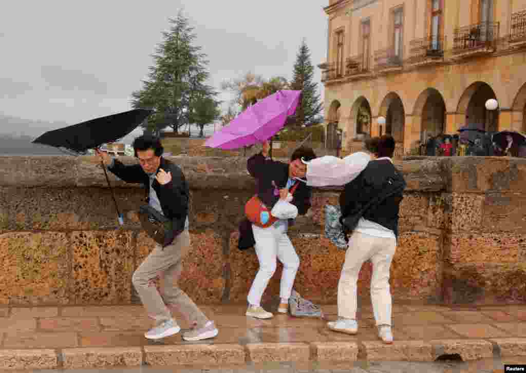 Tourists struggle to hold their umbrellas during heavy rain and high winds as Storm Nelson hits Spain on Easter Sunday, in Ronda.