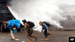 ARCHIVO - Fotógrafos de noticias huyen de un cañón de agua de la policía mientras cubren los enfrentamientos que estallaron en la marcha anual del Primero de Mayo en Bogotá, Colombia, el miércoles 1 de mayo de 2013.