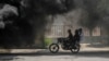 Bodaboda ikipita pembeni mwa moshi uliotokana na mataili yaliyochomwa moto huko Port-au-Prince Agosti14, 2023. Picha na Richard PIERRIN / AFP.
