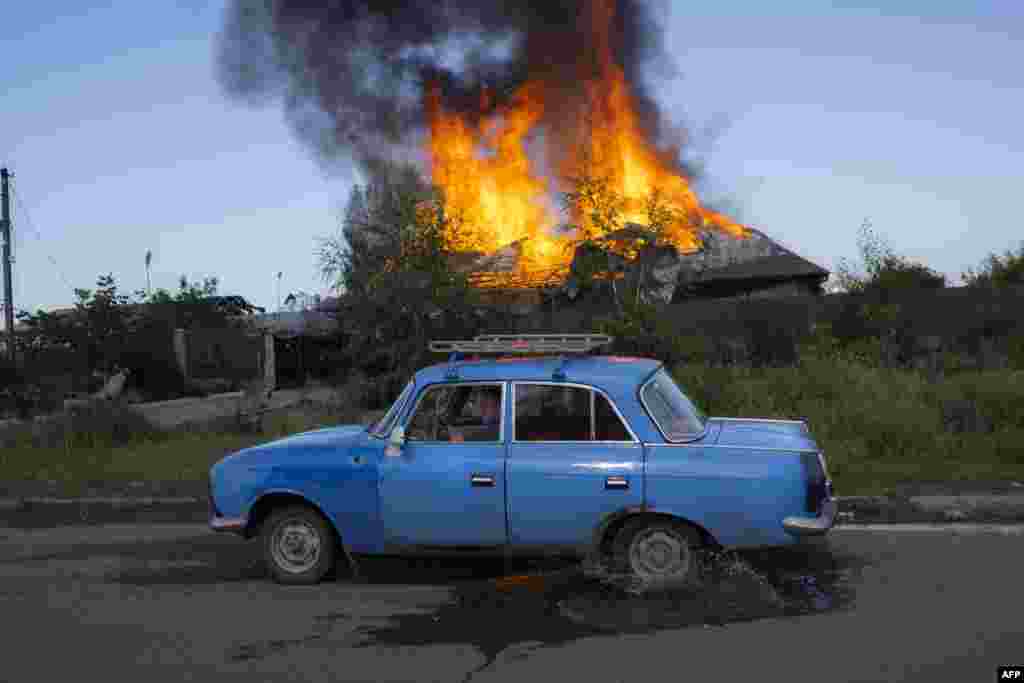 A Ukrainien man drives past a burning house hit by a shell in the outskirts of Bakhmut, eastern Ukraine, amid the Russian invasion of Ukraine.
