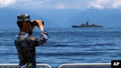 FILE - In this photo provided by China's Xinhua News Agency, a People's Liberation Army member looks through binoculars during military exercises as Taiwan's frigate Lan Yang is seen at the rear, Aug. 5, 2022. (Lin Jian/Xinhua via AP)