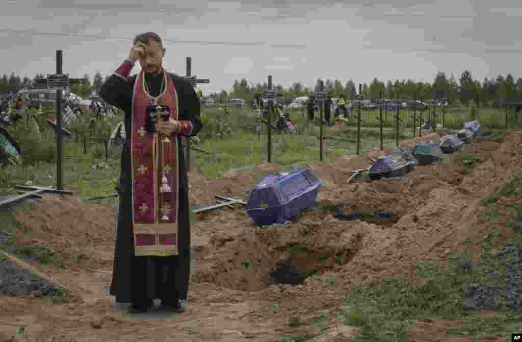 A priest prays for unidentified civilians killed by Russian troops, in Bucha, on the outskirts of Kyiv, Ukraine.