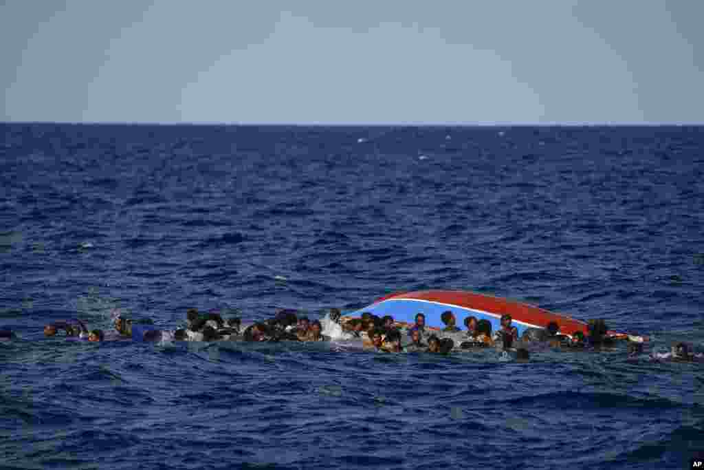 Migrants swim next to their overturned wooden boat during a rescue operation by Spanish NGO Open Arms south of the Italian island of Lampedusa in the Mediterranean Sea.