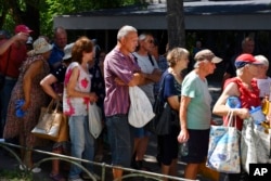 People wait in a line to receive food at a humanitarian aid distribution point in Zaporizhzhia, Ukraine, Aug. 9, 2022.