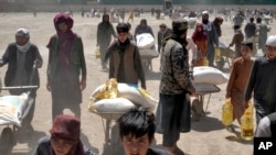 ARCHIVO - Un combatiente talibán hace guardia mientras las personas reciben raciones de alimentos distribuidas por un grupo de ayuda humanitaria chino, en Kabul, Afganistán, el 30 de abril de 2022.