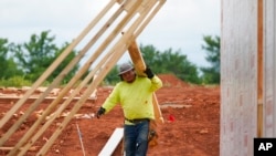 FILE - A worker carries a board at a home construction site June 29, 2021, in Piedmont, Okla.