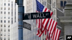 FILE - The Wall St. street sign is framed by the American flags flying outside the New York Stock exchange, Jan. 14, 2022, in the Financial District. The Dow Jones Industrial Average slumped more than 900 points April 28 as another sharp sell-off led by 