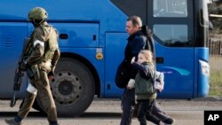 Жители Мариуполя, покинувшие убежище на металлургическом комбинате «Азовсталь», идут к автобусу в сопровождении военнослужащего российской армии (AP)