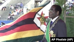 Zimbabwean President Robert Mugabe, sings the national anthem with the national flag in the background during Independence celebrations in Harare, Zimbabwe, Friday, April 18, 2003.