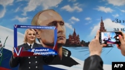 Женщина позирует перед изображением Владимира Путина на уличной стене во время выборов на участке в Донецке, 15 марта, 2024 года