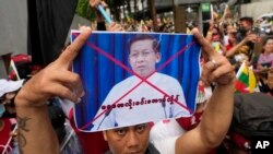FILE - A Myanmar nationals living in Thailand holds a picture of Senior Gen. Min Aung Hlaing, head of the military council as they protest outside Myanmar's embassy in Bangkok, Thailand, July 26, 2022. 
