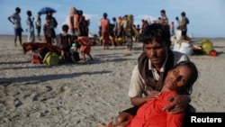FILE - Arif Ullah, who said his village was burnt down and relatives killed by Myanmar soldiers, comforts his wife Shakira who collapsed from exhaustion as Rohingya refugees arrive by a wooden boat from Myanmar to the shore of Shah Porir Dwip, in Teknaf, near Cox's Bazar in Bangladesh, Oct. 1, 2017.