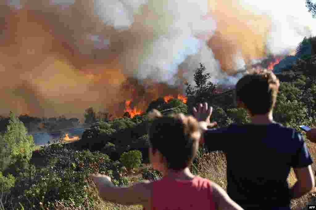 Pedestrians look at a forest fire near Gignac, southern France, July 26, 2022, as the country experiences a dry summer and wildfires destroy many forests across France.