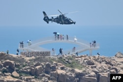 Tourists look on as a Chinese military helicopter flies past Pingtan island, one of mainland China's closest point from Taiwan, in Fujian province, Aug. 4, 2022, ahead of massive military exercises off Taiwan. (Photo by Hector RETAMAL / AFP)