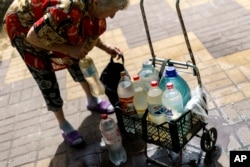 Lyubov Mahlii, 76, packs a crate with water bottles she filled up at a public tank to take back to her apartment in Sloviansk, Donetsk region, eastern Ukraine, Saturday, Aug. 6, 2022. " (AP Photo/David Goldman)