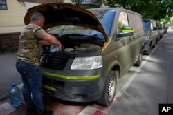 A volunteer puts water to a van motor before heading to delivered goods to soldiers fighting on the eastern and southern fronts, dispatched from an NGO storage center in Kyiv, Ukraine, Monday, June 13, 2022. (AP Photo/Natacha Pisarenko)