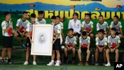 FILE - Coach Ekkapol Janthawong, left, and the 12 boys show their respect and thanks as they hold a portrait of Saman Gunan, the retired Thai SEAL diver who died during their rescue attempt, during a press conference in Chiang Rai, northern Thailand, Wednesday, July 18, 2018. 
