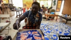 Senegalese artist Omar Ba signs his name on a painting of orange leaves in his studio in Bambilor, Senegal on March 12, 2021. (REUTERS/Cooper Inveen)