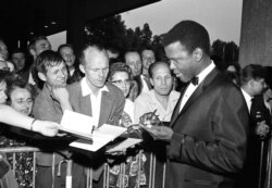 FILE - Sidney Poitier signs autographs before the opening of the 14th International Film Festival at the West Berlin congress hall in Berlin, June 26, 1964.