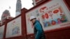 建筑工人走过北京一个居民小区外面，墙上有宣传牌《社会主义核心价值观：富强》《社会主义核心价值观：民主》（2016年12月13日）