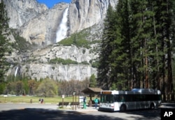 This April 2013 photo shows the bus at Yosemite National Park picking up passengers at Sentinel Bridge, with Yosemite Falls in the background.
