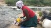 For Chipo Masvinga, the right to water in Zimbabwe’s constitution since 2013 is still far away, with infant daughter Esther and 4-year-old son Emmanuel, she does laundry in Mukuvisi river in Harare, March, 2017. (C. Mavhunga/VOA)