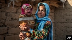 Qandi Gul holds her brother outside their home housing those displaced by war and drought near Herat, Afghanistan. Dec. 16, 2021. Gul’s father sold her into marriage without telling his wife, taking a down-payment so he could feed his family. (AP Photo/Mstyslav Chernov)
