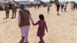 FILE - A man walks with a child through Fort Bliss' Doña Ana Village where Afghan refugees were being housed, in New Mexico, Sept. 10, 2021. 