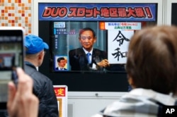 People watch a TV screen showing the name of new era “Reiwa” is unveiled in a news program in Tokyo, Monday, April 1, 2019.