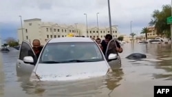 In this video grab from AFPTV, people push a stranded car along a flooded street in Dubai on April 16, 2024.