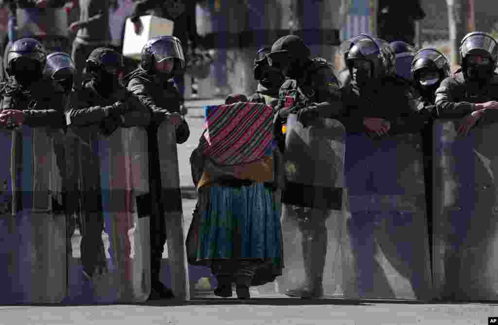 Police make way for an older woman to pass through as they guard the new coca leaf market on the third day of clashes with coca farmers in La Paz, Bolivia, Aug. 3, 2022.