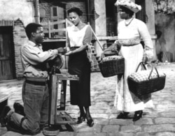 FILE - Kneeling on his crippled legs, Porgy, played by Sidney Poitier, urges Bess (Dorothy Dandridge, center) to join Maria (Pearl Bailey) at the picnic which was to change their lives, in this scene from the movie version of “Porgy and Bess” in character
