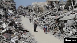 Palestinians walk past the ruins of houses and buildings destroyed during Israel’ military offensive, in the northern Gaza Strip