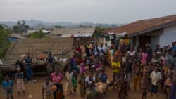 Marie, center left, sits on a bench with a friend as they look towards a drone photographing them in Komao village outskirts of Koidu, district of Kono, Sierra Leone, Sunday, Nov. 22, 2020.