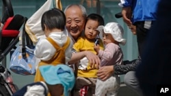An elderly man plays with children near a commercial office building in Beijing on May 10, 2021. (AP Photo/Andy Wong)