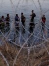 FILE - Migrants wait to climb over concertina wire after they crossed the Rio Grande and entered the US from Mexico, Sept. 23, 2023, in Eagle Pass, Texas.