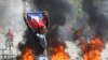 Seorang demonstran mengibarkan bendera Haiti dalam aksi protes meminta peungunduran diri Perdana Menteri Ariel Henry di Port-au-Prince, pada 1 Maret 2024. (Foto: AP/Odelyn Joseph)