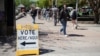 People walk past a bilingual sign directing voters to a polling place at the Arizona State University Downtown Campus A.E. England building as the Democratic and Republican parties hold primary elections in Phoenix, Arizona, March 19, 2024. 